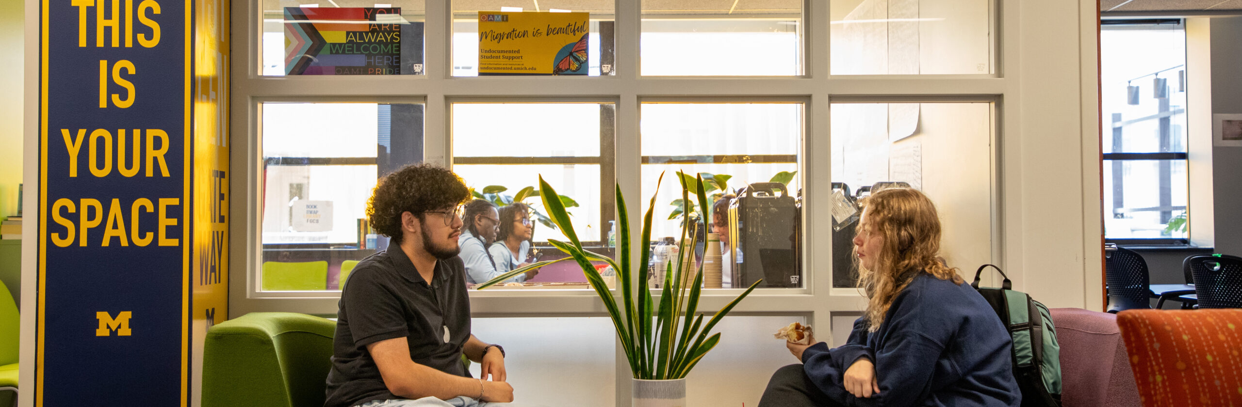 Two students sitting on couches facing each other with a sign that says 