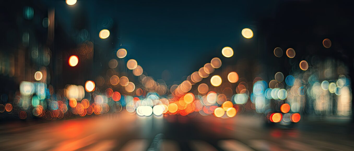 Blurred bokeh lights of a city street at night, with car headlights and taillights creating streaks of color.