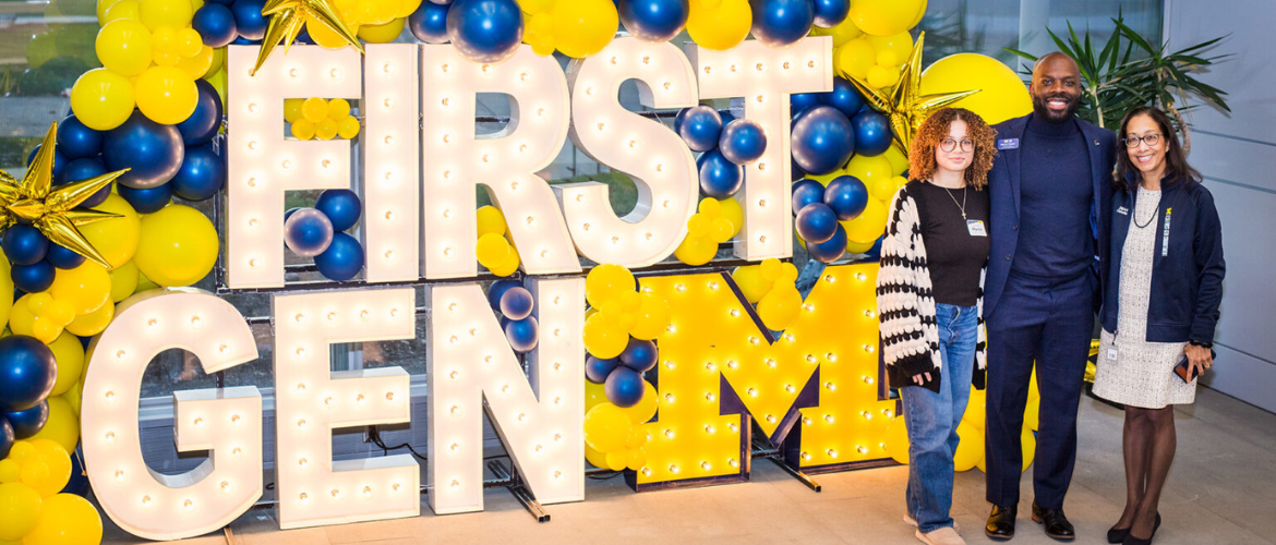 Three people stand in front of large marquee letters spelling 
