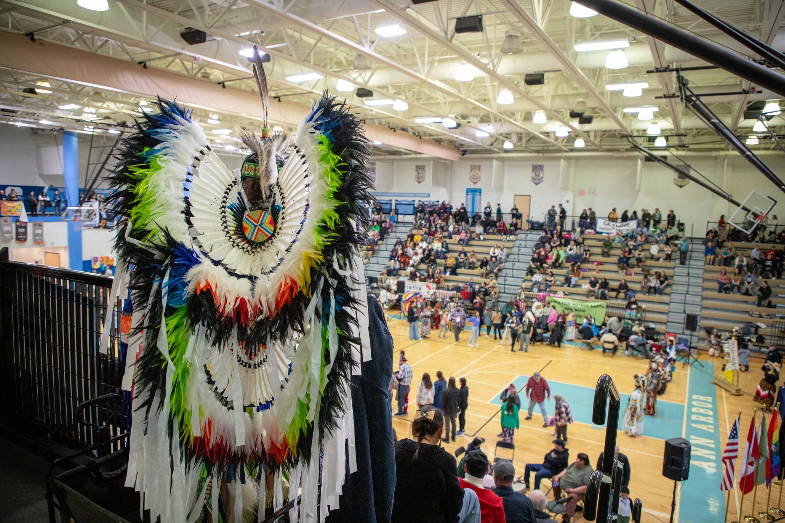 person in regalia from behind standing looking down at gym floor