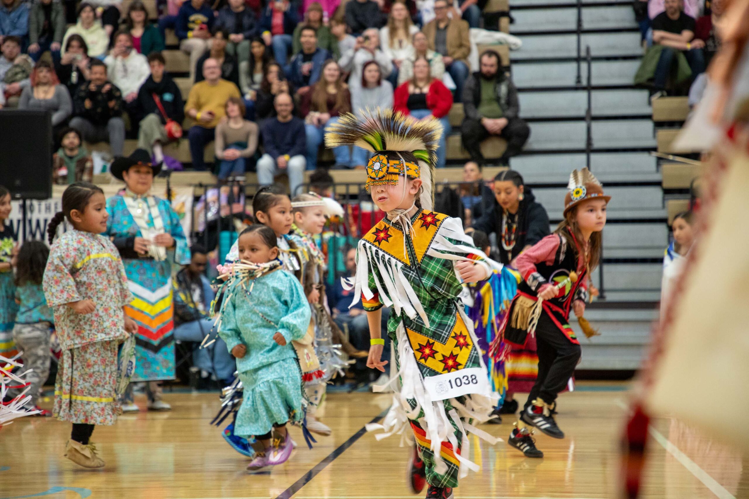 group of people dancing in a gym wearing regalia