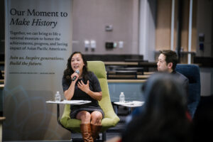 female speaker seated in green chair holding microphone with. male to her right