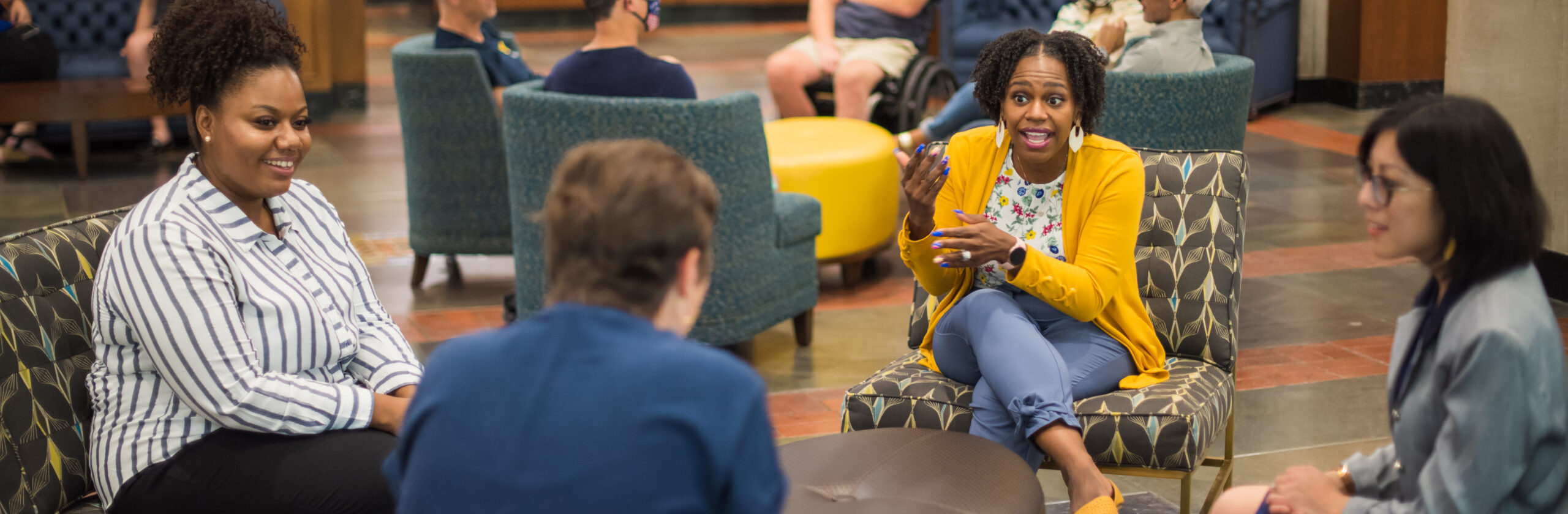 four people seated in large arm chairs in conversation